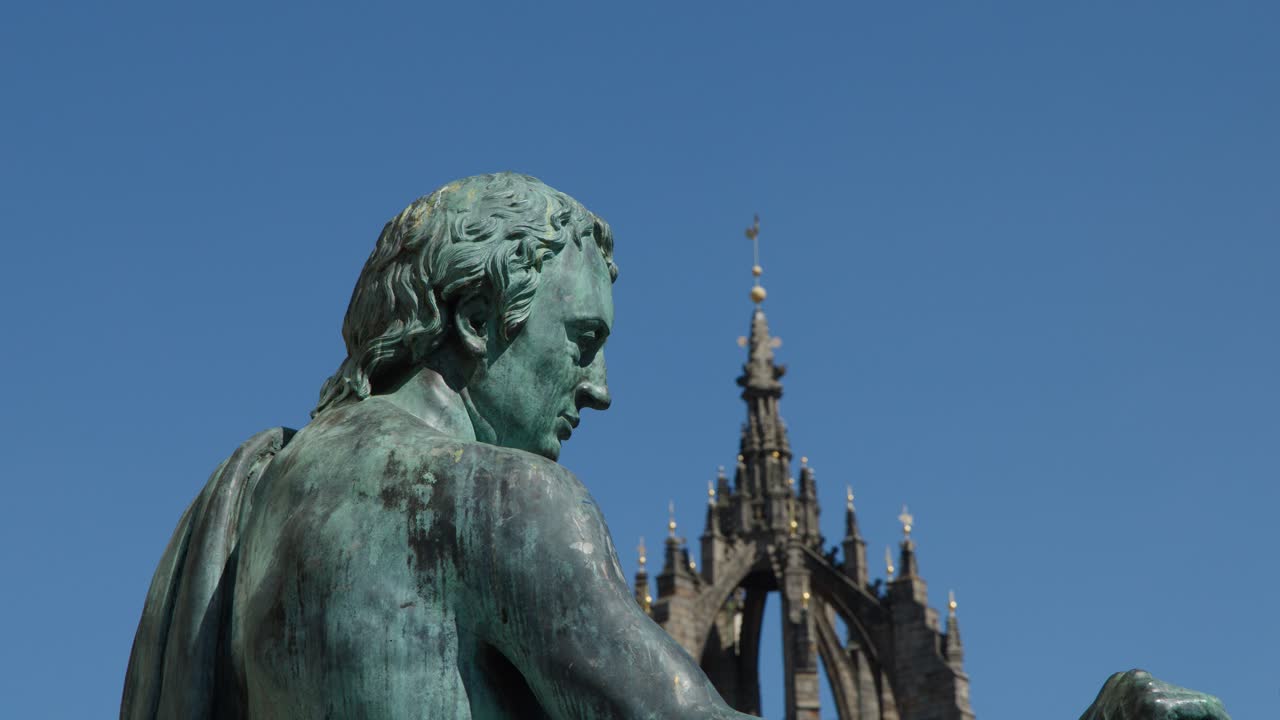 Slow pan across bronze philosopher statue with cathedral spire, clear daylight, blue sky background