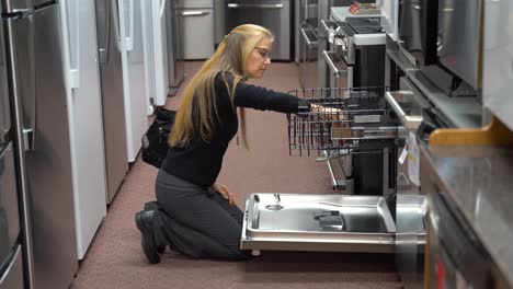 una revelación que muestra a una mujer rubia bastante madura mirando lavavajillas en una tienda de electrodomésticos de cocina