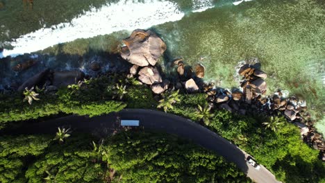 low drone shot of passing cars on road near cliff, huge granite rock at anse forbans beach mahe seychelles