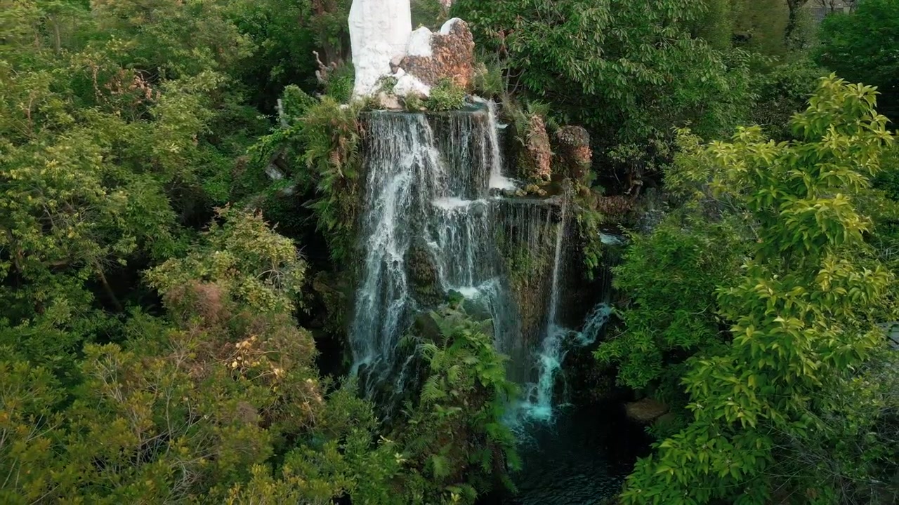Cascata artificiale che scende da una parete rocciosa in un lussureggiante giardino verde.