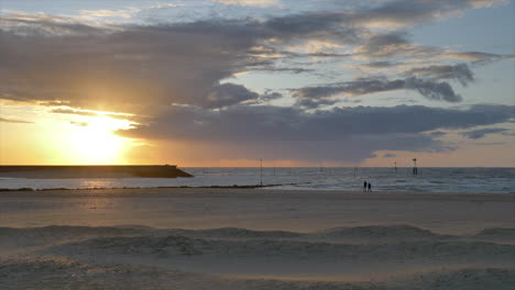 Wunderschöne-Strandlandschaft-In-Goldener-Stunde,-Silhouetten-Von-Menschen,-Die-Spazieren-Gehen