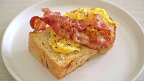 pan tostado con huevos revueltos y tocino en un plato blanco
