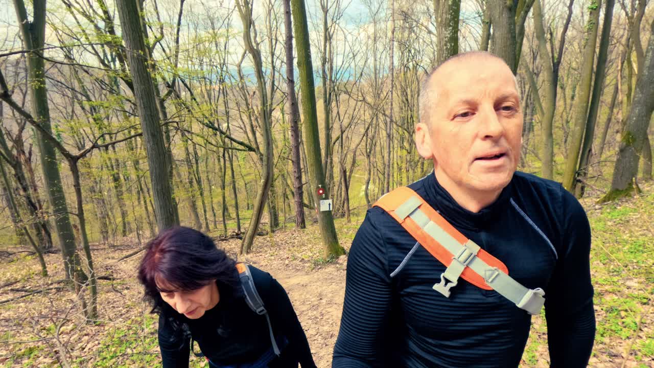 Coppia di mezza età che fa trekking insieme in un bosco fiorito primaverile. Concetto di invecchiamento sano, rimanere attivi, forma fisica e vitalità nella natura.