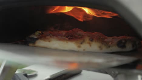 removing baked pizza, with ham, cheese and pesto from oven