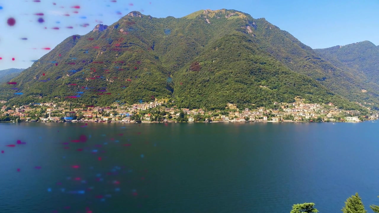 Puntini rosso-blu appaiono a sinistra e si spostano al centro, poi a destra, rivelando una montagna e una città costiera.