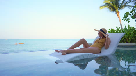 happy pleased asian woman laying on bed in infinity pool and enjoying alone in view on sea horizon, static shot with copy space