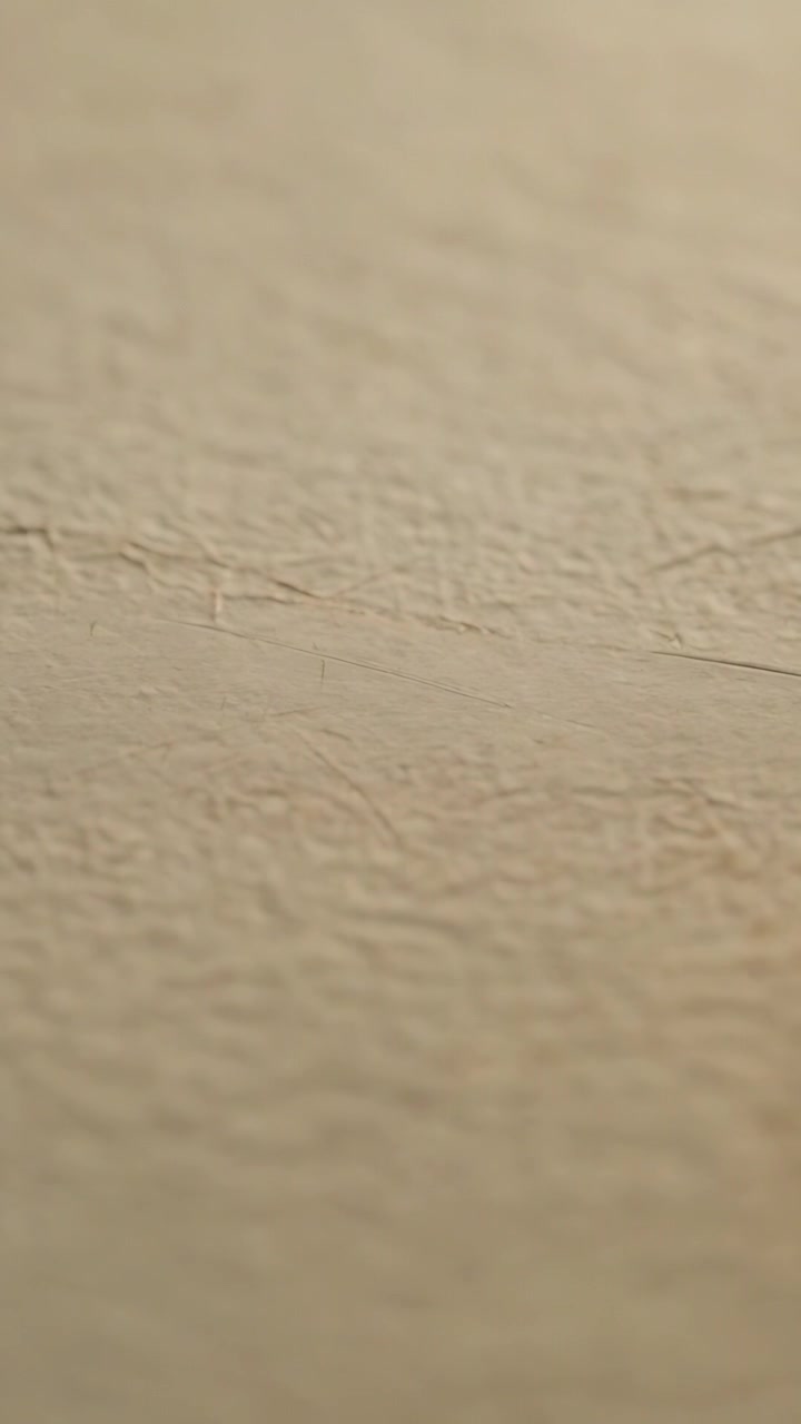 Vertical video: Shifting camera drifting over textured beige wall, revealing texture details, seam