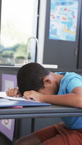 vertical video: in school, boy resting head on desk, feeling tired in classroom