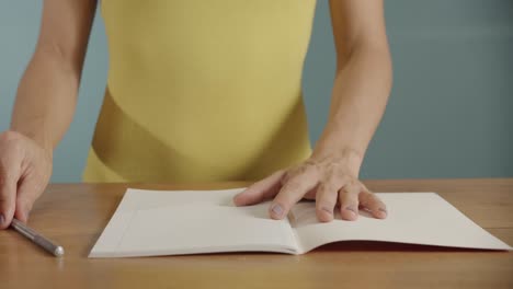 Close-up-shot-of-woman's-hands-drawing-a-heart-on-a-white-paper-notepad-with-a-pencil