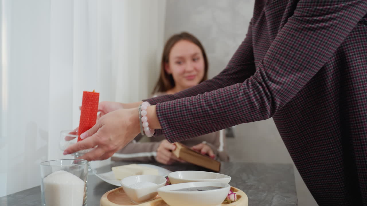어린 소녀는 부드러운 색 커튼 근처에 앉아서 책을 평화롭게 읽고, 그녀의 여동생은 저녁 테이블에 은 불을 놓고 편안한 저녁을 준비합니다.