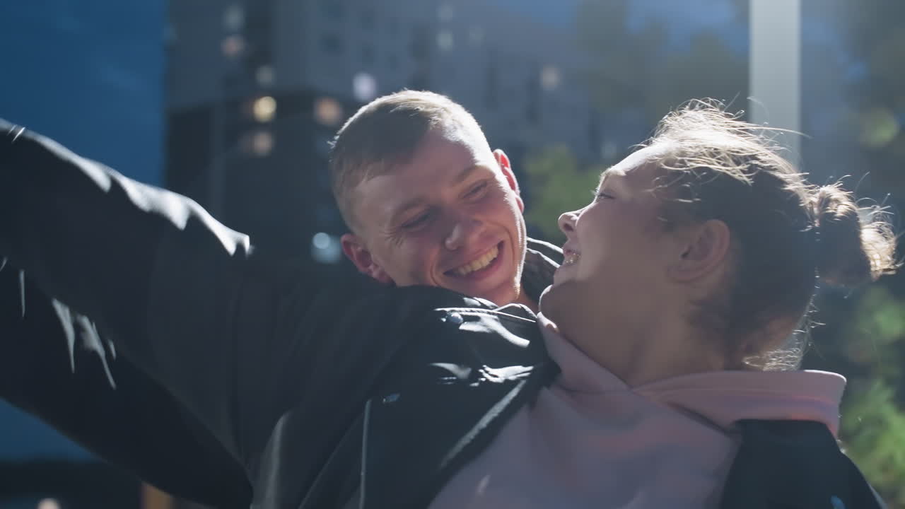 Close-up of woman looking lovingly at her man as they dance under street light with soft light reflecting on their faces, residential building and city lights softly glowing in background