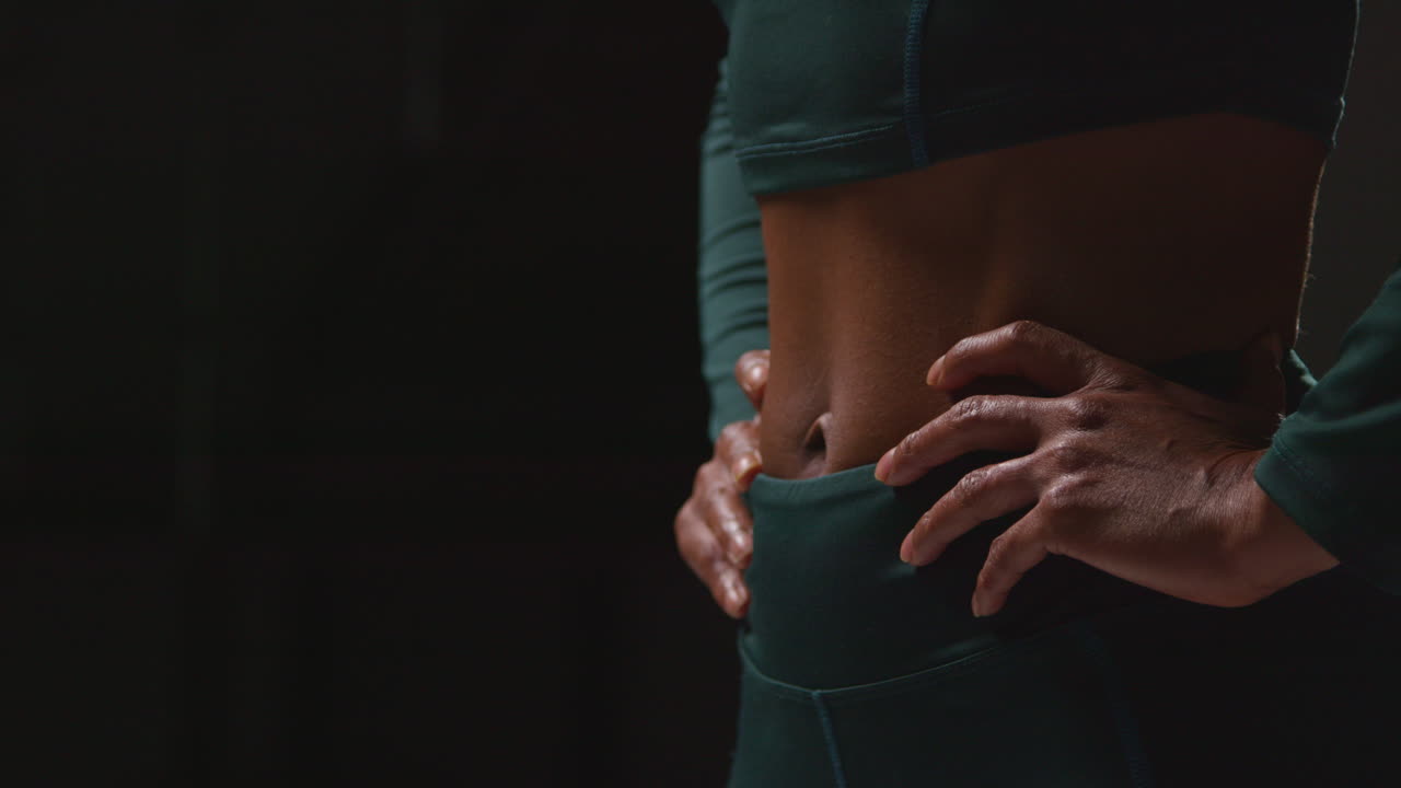 Close Up Showing Toned Stomach Of Female Athlete Wearing Tracksuit Training Shot Against Black Background