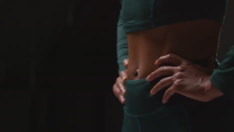 Close-Up-Showing-Toned-Stomach-Of-Female-Athlete-Wearing-Tracksuit-Training-Shot-Against-Black-Background