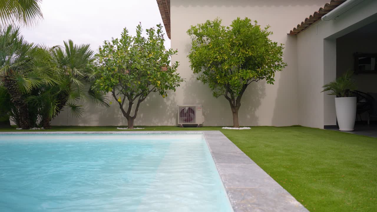 Modern backyard with a serene swimming pool, lush trees, and an air conditioning unit. Ideal for home, garden, or outdoor living concepts.