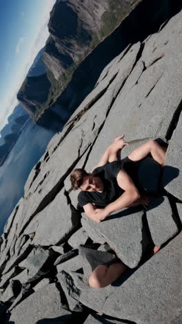 man rock climbing on a cliff face overlooking a scenic fjord