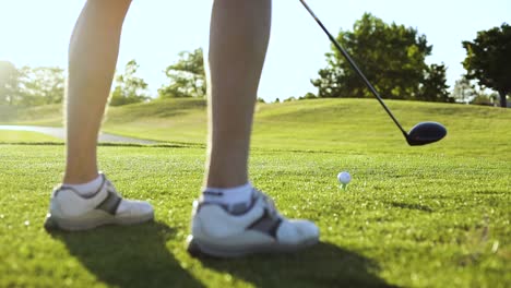 low-angle shot behind a golfer's legs showing that he is about to drive his ball from the tee box