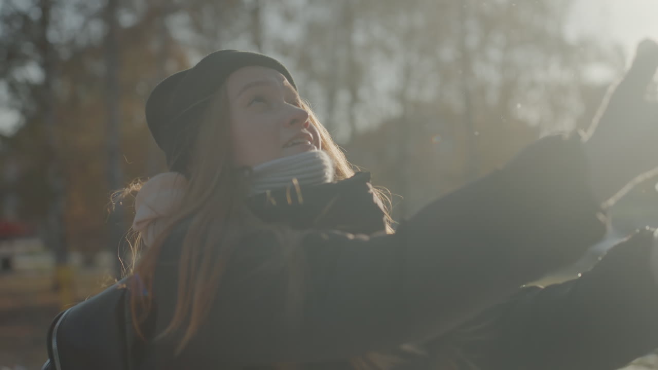 Sunlit park white woman tossing snow, college student enjoying afternoon play, closeup smiles with scarf and beanie, rimlight on red hair, candid energy, soft bokeh and chilly breath