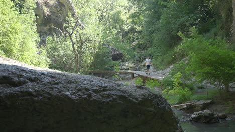 Local-tourist-walking-on-a-wooden-ramp-going-to-the-entrance-of-the-cave-under-the-natural-arch-locally-known-as-God's-Bridge,-located-near-Vratsa,-in-Bulgaria