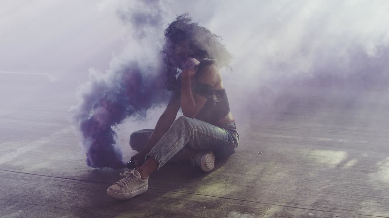 hermosa mujer joven modelando con una granada de humo púrpura en una iluminación dramática de mal humor