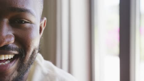 Video-portrait-of-half-the-face-of-happy-african-american-man-smiling-at-home,-with-copy-space