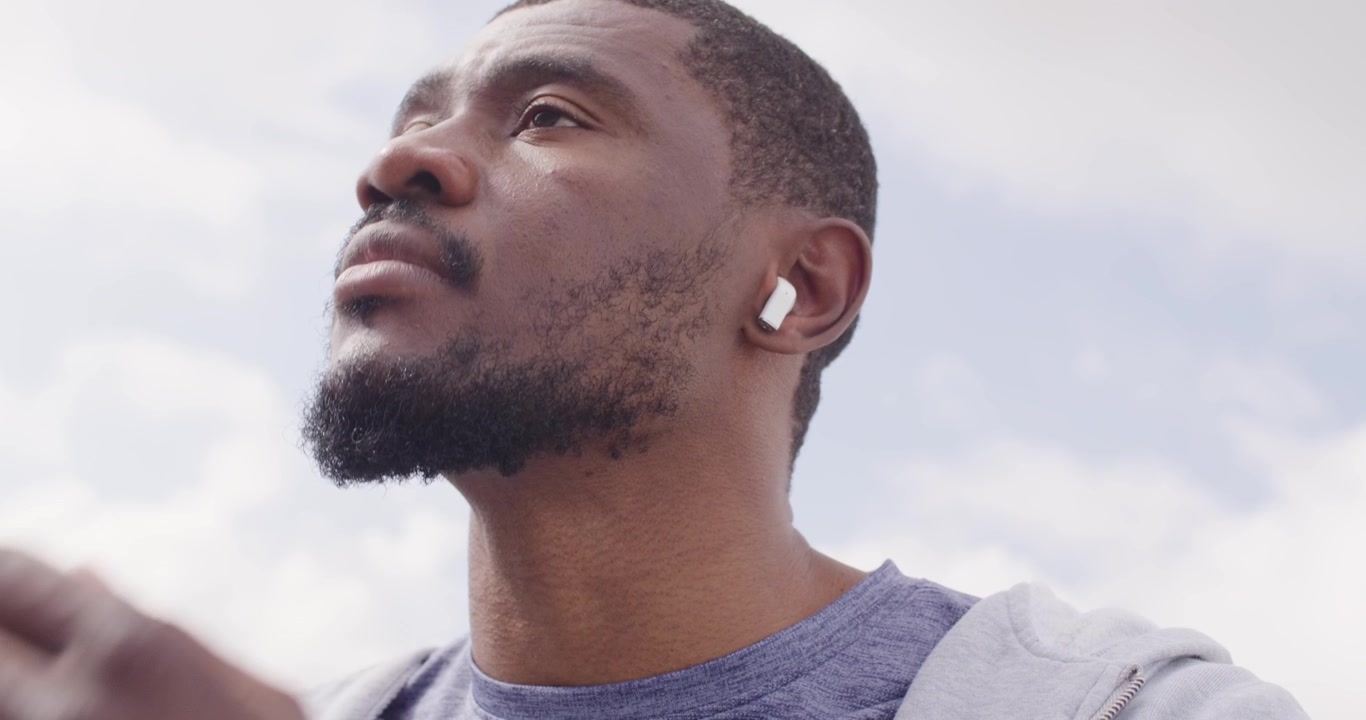 30s African man checking white earbuds wearing smartwatch on balcony, placing, adjusting to listen