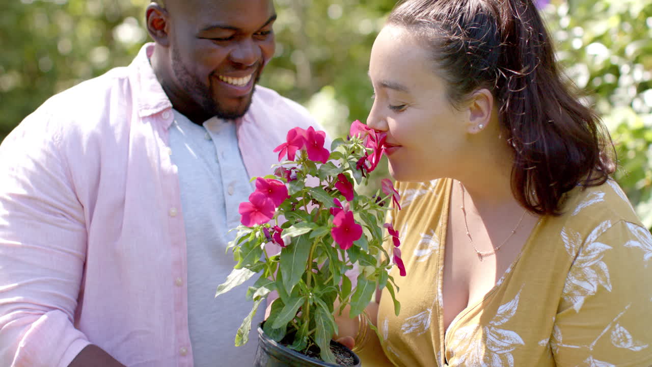 African American male and Caucasian female friends smelling flowers in backyard garden