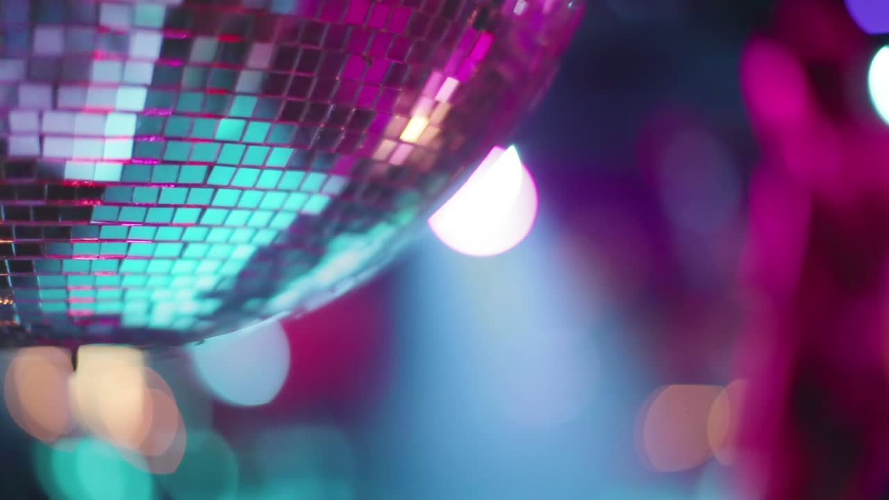 Næroptagelse af en diskokugle, der reflekterer levende pink og lilla lys, med farverige bokeh-effekter i baggrunden. De spejlblanke fliser glimter dynamisk og skaber en festlig og livlig stemning.