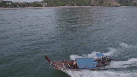 a long tailed tourist boat speeds along the waters of railey beach, krabi, thailand