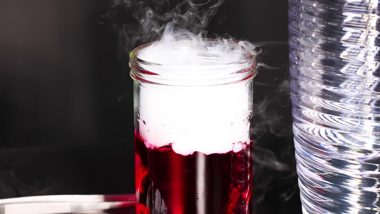 활기찬 화학 반응은 통제된 환경에서 포착 된 유리 항아리에 있는 은 액체에서 연기가 나옵니다.