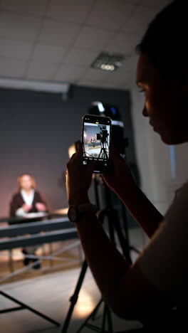 woman takes photos of a lady sitting at desk in modern photo studio. backstage of the footage of blog. vertical video