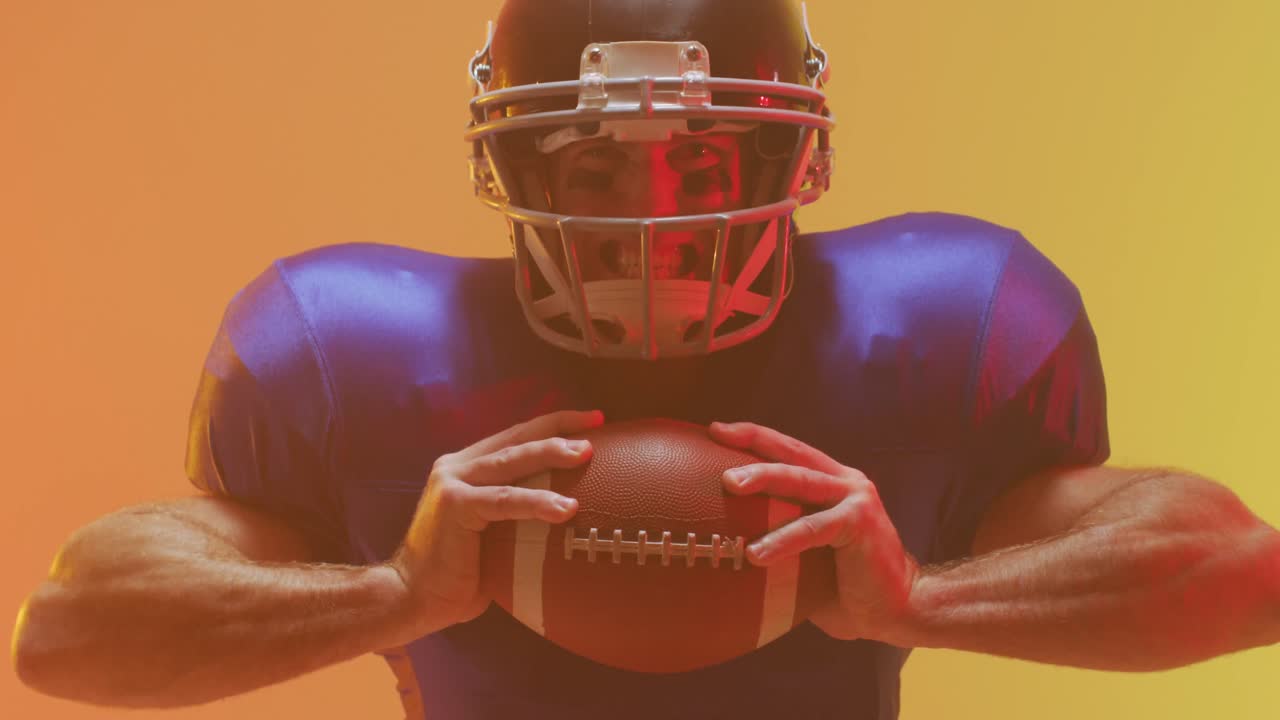 Video ravvicinato di un giocatore di football americano caucasico con casco e pallone su sfondo arancione.