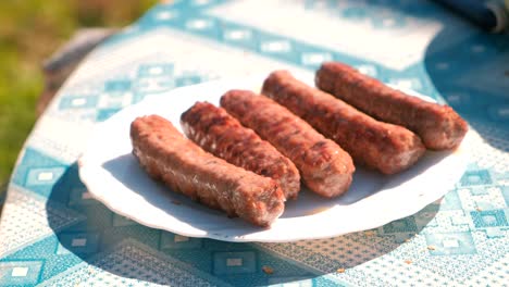 man puts sausages on a plate from the grill with a knife. close-up hands.
