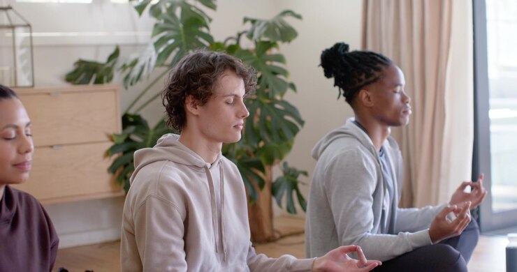Diverse trio meditating on mats in living room following guided cue for calm with water bottle