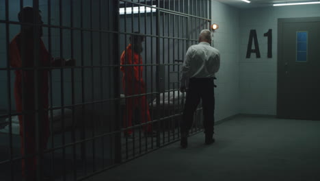 prison officer with police baton watches criminals in prison cells