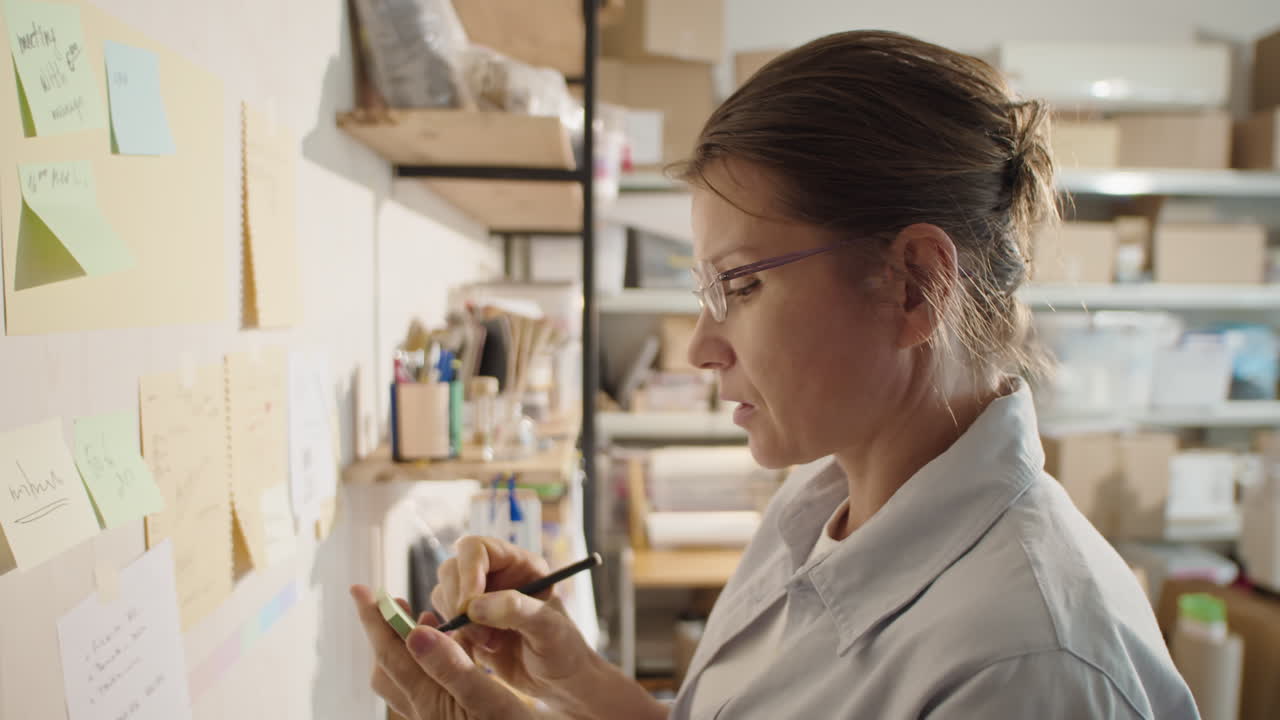 Woman Attaching Sticky Notes to Wall in Workshop