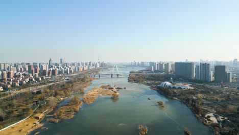 Plataforma-Rodante-Aérea-Panorámica-Sobre-El-Río-Benghe-Y-El-Centro-De-La-Ciudad-De-Linyi-Conectados-Por-Un-Puente