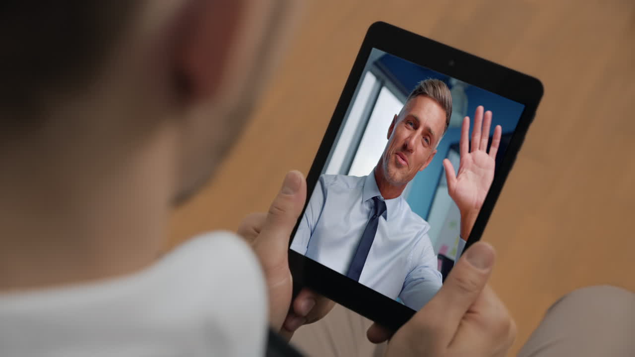 Primo piano di un capo che parla durante una videoconferenza online con un uomo sconosciuto che tiene in mano un tablet in ufficio