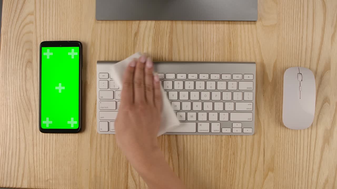 A woman sprays an antiseptic on a napkin and wipes a computer keyboard. Smartphone with green screen and chroma key with vertical screen position. Hands close up. Slow motion