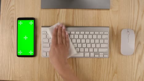 una mujer pulveriza un antiséptico en una servilleta y limpia un teclado de computadora. teléfono inteligente con pantalla verde y tecla cromática con posición vertical de la pantalla. manos cerca. cámara lenta