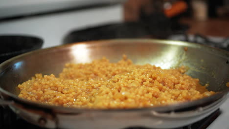 Couscous-Köchelt-Und-Brutzelt-In-Einer-Pfanne-Auf-Dem-Herd,-Während-Dampf-In-Zeitlupe-Aufsteigt