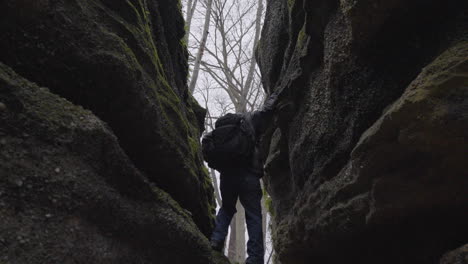 un excursionista desciende por una grieta rocosa presionando contra las paredes rocosas y bajándose hasta el suelo del bosque cubierto de hojas