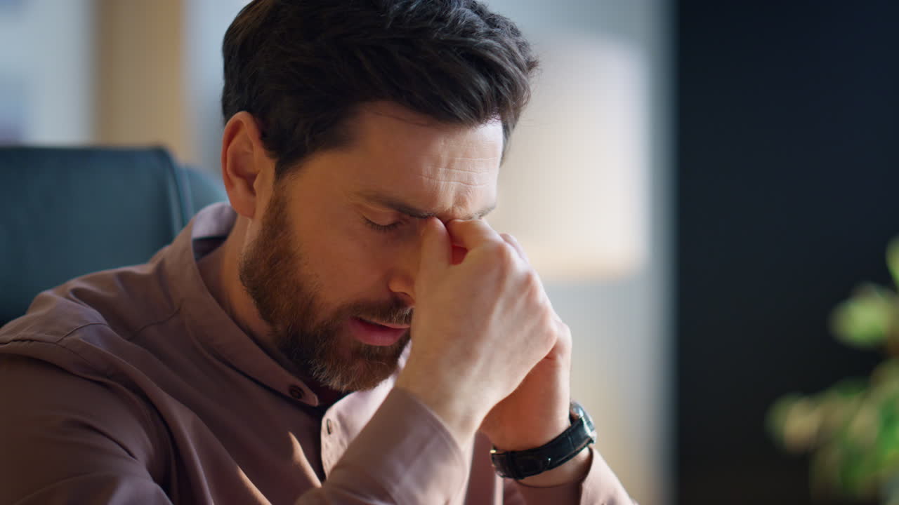 Overworked man calling telephone suffering from headache at workplace close up.