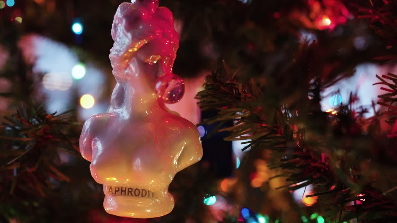 Aphrodite blowing bubble gum small statue hanging on fake Christmas Tree, slomo handheld push in.