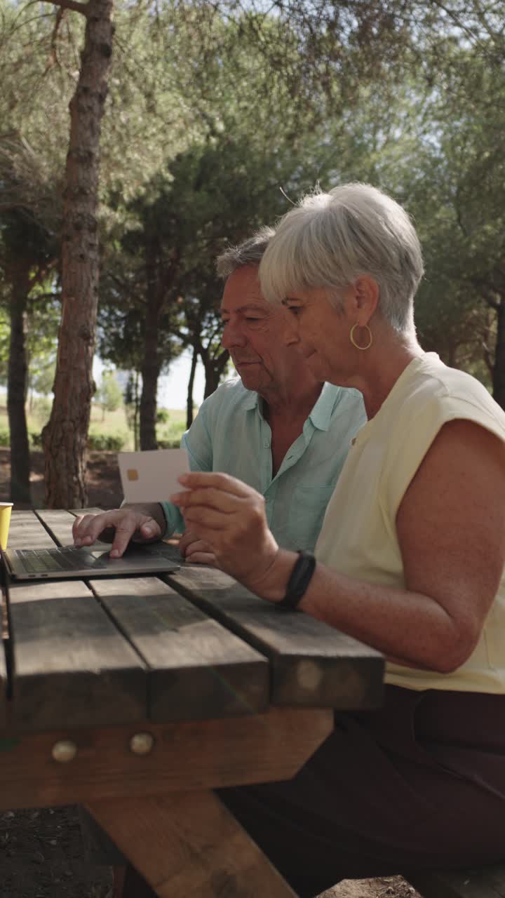Senior couple using a laptop for online shopping at a picnic table