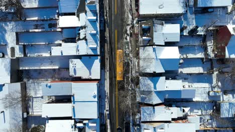 yellow school bus driving on narrow road of american city in winter snow