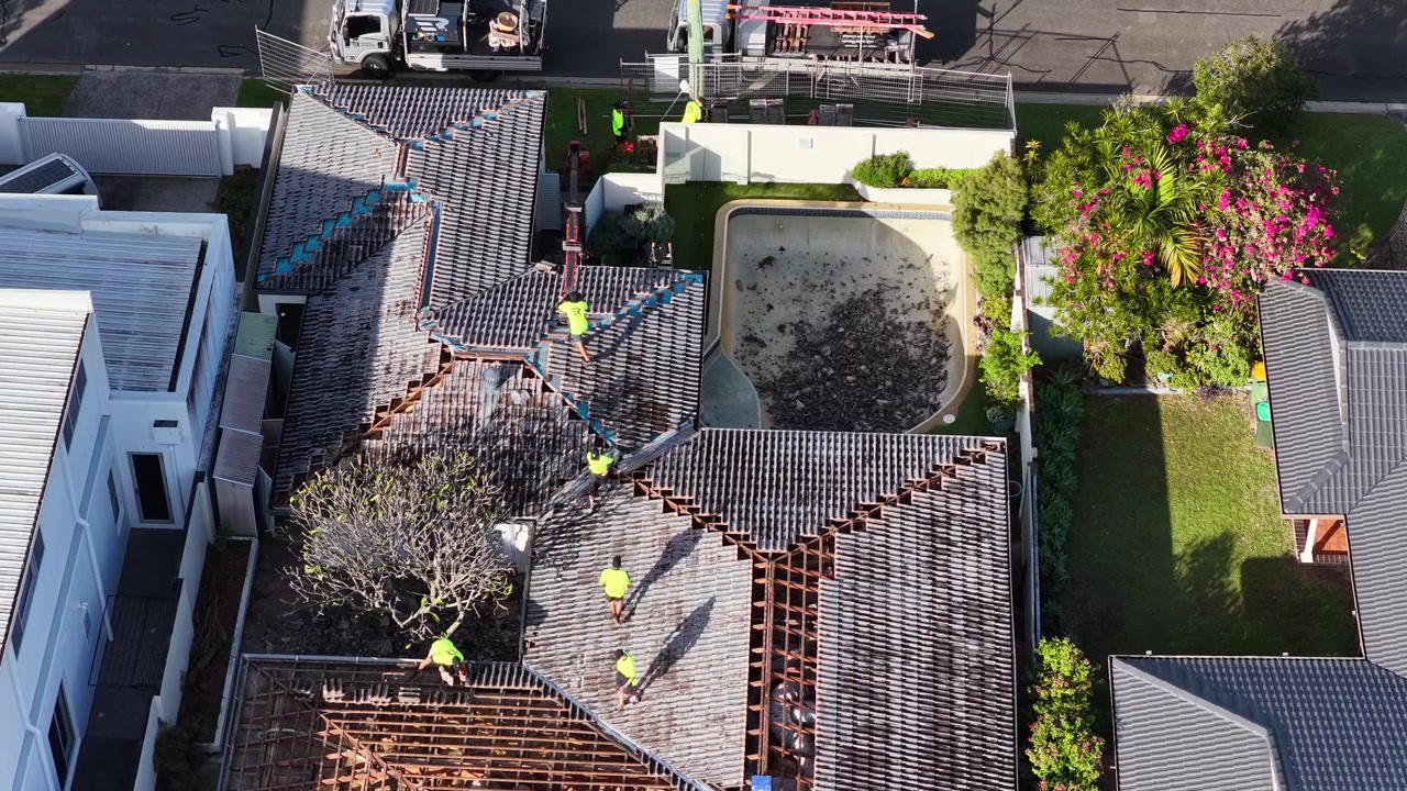 High-angle drone shot of contractors in hi-vis vests replacing tiles on a residential roof.