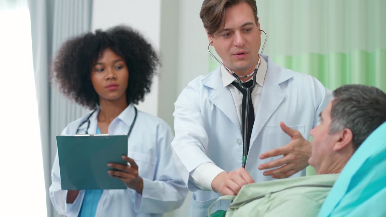 Doctor and assistance nurse visit patient in the room and using stethoscope checking up heart beat rate. Older man lying on the bed and breathe in and breathe out during doctor listening.