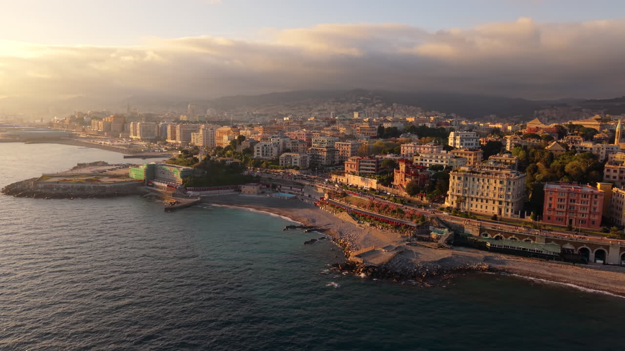 Panoramica aerea della costa di Genova con spiaggia ed edifici cittadini illuminati dalla calda luce dell'alba