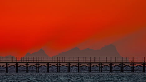 el lapso de tiempo de las montañas silueta y el sol naciente contra el cielo rojo vibrante