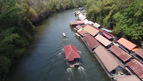 A-floating-house-is-sailing-past-a-charming-small-floating-village-in-the-middle-of-the-jungle-of-Sai-Yok-National-Park-in-Thailand-in-Southeast-Asia-on-a-clear-blue-day